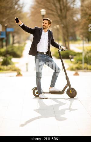 Bel giovane uomo d'affari che usa il telefono cellulare su scooter elettrico Foto Stock