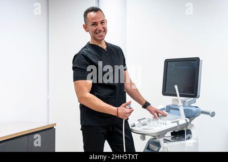 Gineicologo felice in piedi vicino alle apparecchiature mediche in ospedale Foto Stock