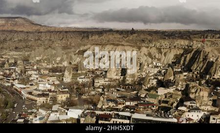 Vista aerea di una piccola città situata presso la catena montuosa. Azione. Bandiera turca rossa che sventola su una cima rocciosa, villaggio soleggiato in zona asciutta Foto Stock