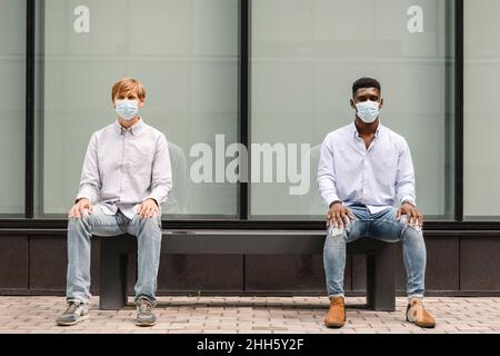 Amici multirazziali con mascherine protettive per mantenere la distanza sociale Foto Stock