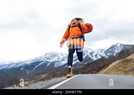 Un escursionista spensierato che salta sulla strada di montagna in inverno Foto Stock