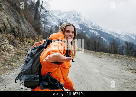 Uomo allegro in giacca arancione che cammina sulla strada di montagna Foto Stock