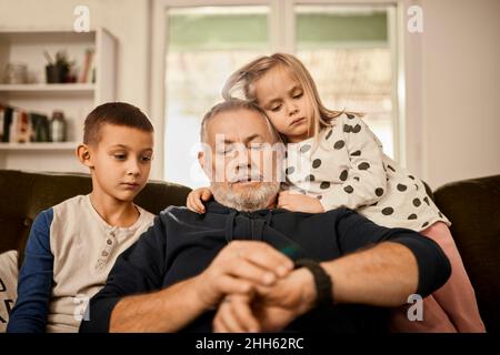 Nonno che usa l'orologio intelligente seduto con i nipoti a casa Foto Stock