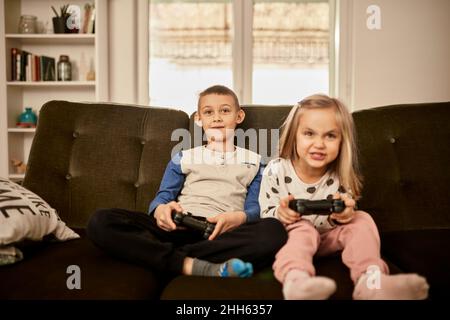 Fratello e sorella giocare video gioco seduto sul divano a casa Foto Stock