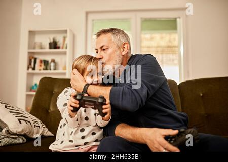 Nonno bacia la nipote tenendo il joystick a casa Foto Stock