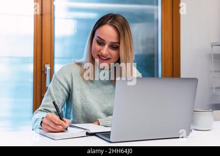 Donna d'affari con computer portatile iscritto in agenda sulla scrivania in studio Foto Stock