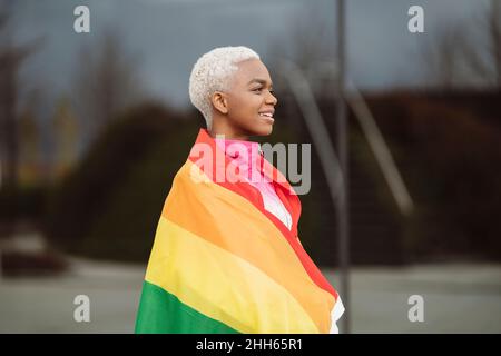 Donna sorridente LGBTQIA avvolta nella bandiera arcobaleno Foto Stock