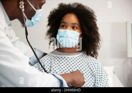Medico che esamina il paziente indossando una maschera protettiva per il viso in ospedale Foto Stock