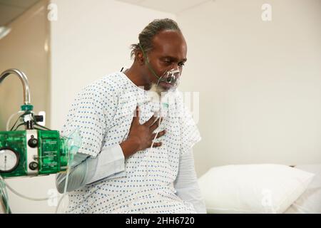 Paziente che tocca il torace indossando la maschera di ossigeno in sala medica Foto Stock