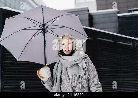 Donna sorridente che tiene l'ombrello in inverno Foto Stock