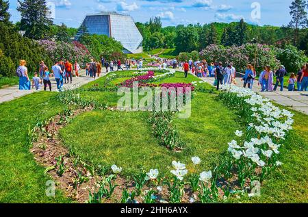 KYIV, UCRAINA - 16 MAGGIO 2021: Il prato verde, tulipani in fiore, lilla e alberi lussureggianti nel Giardino Botanico di Hryshko con una grande serra, visto nel Foto Stock