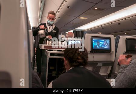 Stewardess che indossa la maschera facciale Covid che serve i clienti in Airliner. Foto Stock