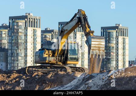 Lavori dell'escavatore sul terreno su sfondo multi-storia case Foto Stock