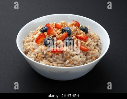 Ciotola di farina d'avena con frutti di bosco su sfondo nero Foto Stock