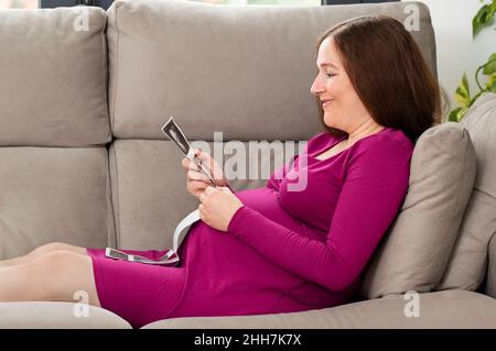 Scatto di una donna incinta che guarda un'immagine del sonogramma a casa Foto Stock