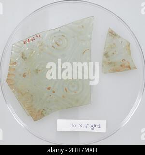 Frammenti di vetro gli scavi copti del 4th secolo del Metropolitan Museum in una necropoli del deserto libico d'Egitto hanno rivelato una cappella funeraria a cupola con una forma intrigante di decorazione: Vasi di vetro di varie forme e colori impressi nell'intonaco della cupola. Questi frammenti provengono da una vasca poco profonda in vetro verde-chiaro con una decorazione stampata di cerchi concentrici all'interno di una scacchiera. Frammenti di vetro 479202 Foto Stock