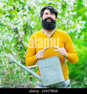 Molla. L'uomo felice con annaffiatura può. Giardiniere bearded prepari a piantare. Agricoltore che lavora in giardino. Foto Stock