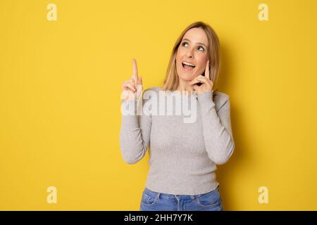 Stupito giovane donna in abbigliamento casual puntando dito in piedi isolato su sfondo giallo. Foto Stock