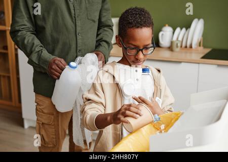 Ritratto di giovane ragazzo afroamericano smistamento rifiuti a casa con padre in background, copia spazio Foto Stock