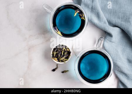Due tazze di vetro con tè blu di anchan da fiore di pea farfalla su sfondo di marmo, vista dall'alto. Foto Stock