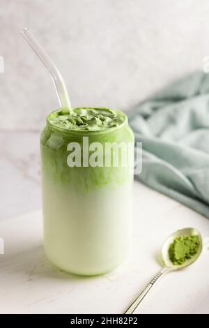 Bicchiere di latte di dalgona matcha e cucchiaio di polvere di tè verde su sfondo bianco. Foto Stock