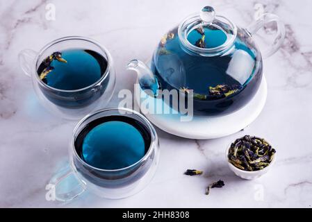 Due tazze e teiera di vetro con tè di fiori di pisello farfalla e clitoria ternatea a secco fiore su sfondo di marmo, bevanda blu alle erbe di anchan. Foto Stock