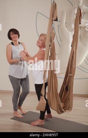 Donna anziana felice e allenatore di yoga di volo ridendo le mani di tenuta dopo l'allenamento divertente Foto Stock