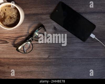 vista dall'alto della tazza da caffè, dei bicchieri e del telefono cellulare che cantano su sfondo di legno scuro Foto Stock