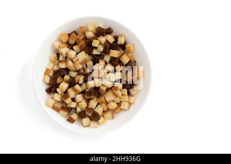 mucchio di crostini fatti in casa isolati su sfondo bianco, vista dall'alto, cubetti di pane croccante, segale secca e briciole di grano in ciotola, crouoton o crac arrosto Foto Stock