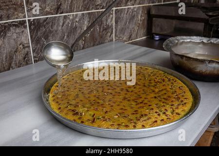 Dessert Kadayif con pistacchio su un vassoio nel laboratorio kadaif, lo chef versa sherbet sul vassoio kadaif appena fatto. Cucina turca kadayif desser Foto Stock