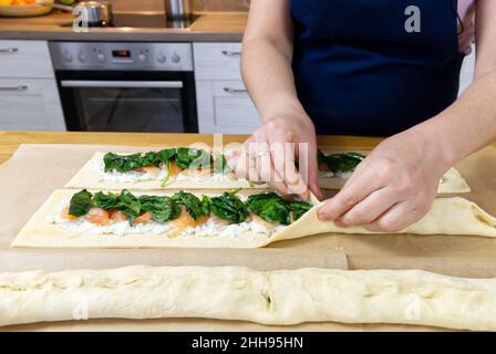 il cuoco mette gli spinaci e la trota sull'impasto. Torta di Natale saporita a forma di un processo di cottura della corona. Foto Stock