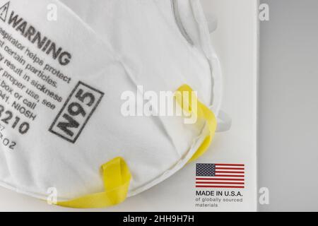 Una maschera facciale N95 su una scatola con un'etichetta Made in USA di materiali di provenienza globale, su sfondo bianco Foto Stock