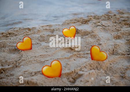 quattro cuori gialli nella sabbia si ergono sul mare Foto Stock