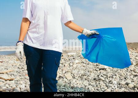 Una donna con una borsa blu vuota su una spiaggia di ciottoli Foto Stock