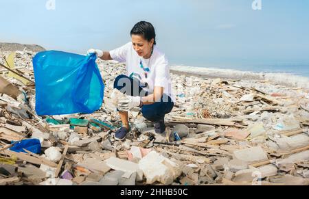 Una donna raccoglie la spazzatura su una spiaggia. Spazio di copia Foto Stock