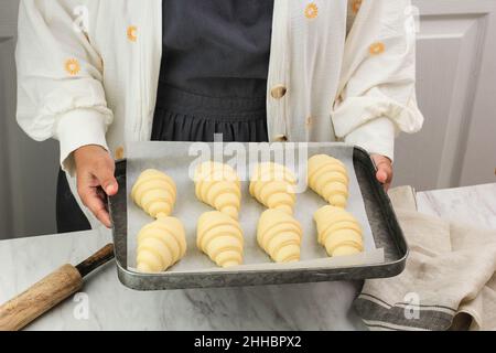 Pasta per croissant. Preparazione dei croissant. Teglia da forno femminile asiatica con croissant crudo, concetto di preparazione della panetteria Foto Stock