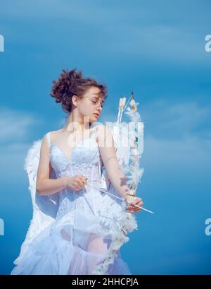 Valentin adolescente ragazza con arco freccia pronta a sparare. Carino angelo teen con le ali di piume sul cielo. San Valentino. Foto Stock