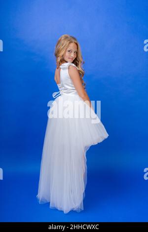 Foto un adorabile angelo scolaretta carino in un abito bianco, su sfondo blu. Caucasica bella ragazza posa felice in studio. Angel bambino Foto Stock