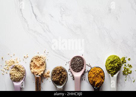 Super alimenti in polvere in cucchiai, sfondo di marmo bianco, spazio copia. Foto Stock