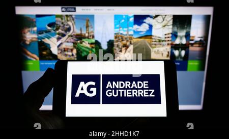 Persona che detiene il cellulare con il logo del conglomerato brasiliano Andrade Gutierrez S.A. sullo schermo di fronte al sito web aziendale. Mettere a fuoco sul display del telefono. Foto Stock