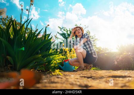 Estate. Una giovane donna sorridente siede in giardino, strofinando il sudore dalla fronte. Stagione di giardinaggio. Spazio di copia. Foto Stock