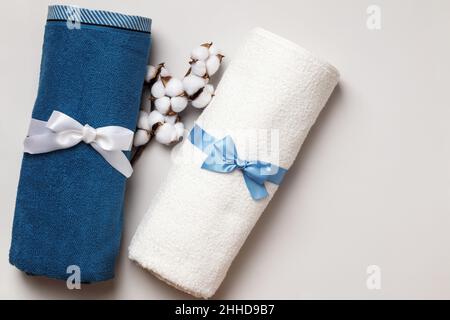 Vista dall'alto degli asciugamani bianchi e blu avvolti in spugna con ramo in cotone su sfondo grigio con spazio per testo e copia. Foto Stock