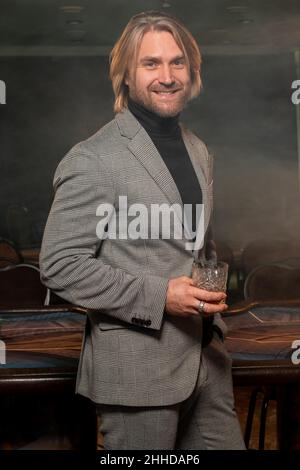 Sorridente uomo barbuto in piedi con un bicchiere di brandy nel casinò Foto Stock