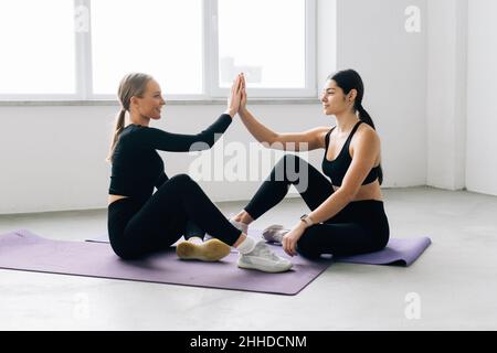 Due ragazze allegre sportswomen si siedono sul pavimento della palestra e si danno cinque a vicenda Foto Stock