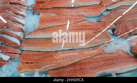 Filetto di salmone fresco crudo su ghiaccio al banco in un negozio di pesce. Filetti di pesce rosso nel frigorifero in vetro sono venduti al supermercato. Foto Stock