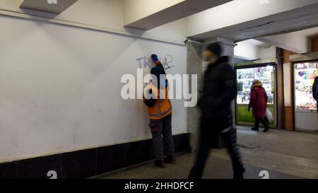 Rimozione dei graffiti dai vandali nel passaggio sotterraneo. Dipendente della città, indossando una uniforme arancione, pulisce le pareti dai graffiti e dalla scrittura, con un rosso Foto Stock