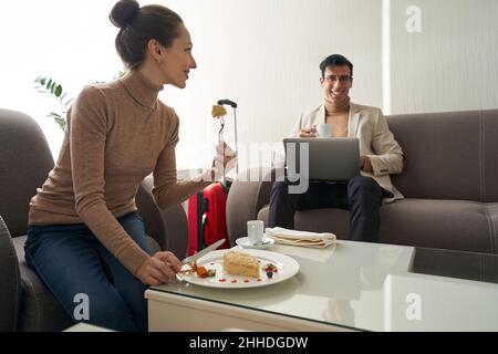 Donna che mangia la torta e guarda l'uomo con il portatile Foto Stock