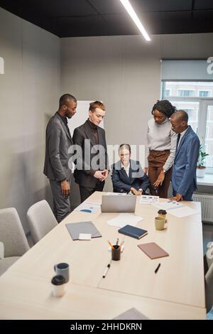 Ritratto verticale di una donna d'affari di successo che utilizza la sedia a rotelle mentre conduce l'incontro con il team in ufficio Foto Stock
