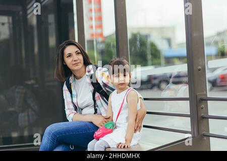 Una giovane donna con sua figlia è in attesa di un autobus pubblico alla stazione degli autobus Foto Stock