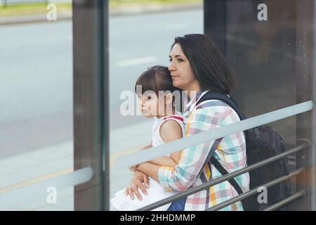 Una giovane donna con sua figlia è in attesa di un autobus pubblico alla stazione degli autobus Foto Stock